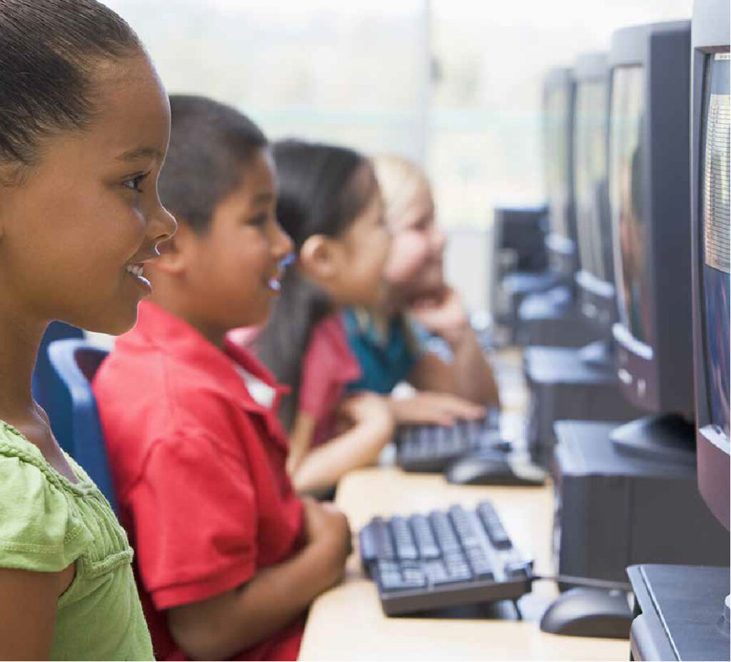 Row of children working on computers and smiling.