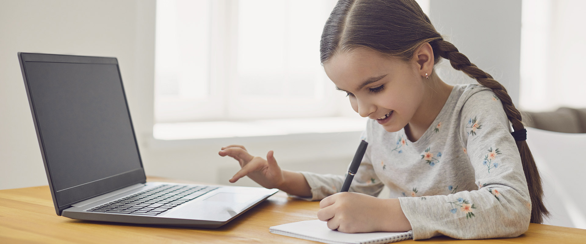 Little girl with pigtails writing and using a laptop