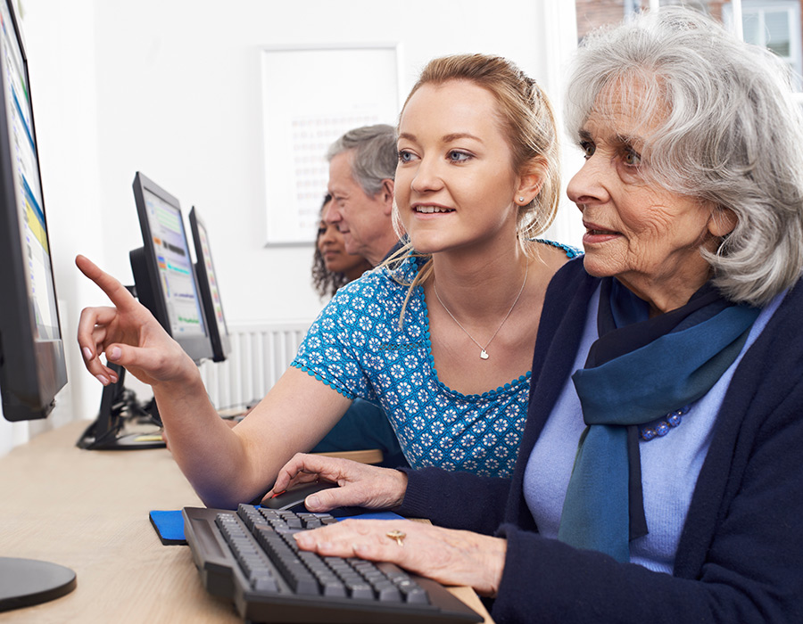 Woman helping an older lady learn how to use a computer