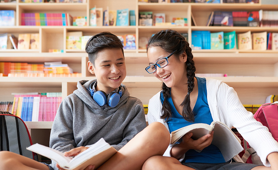 Teens reading books next to eachother and smiling