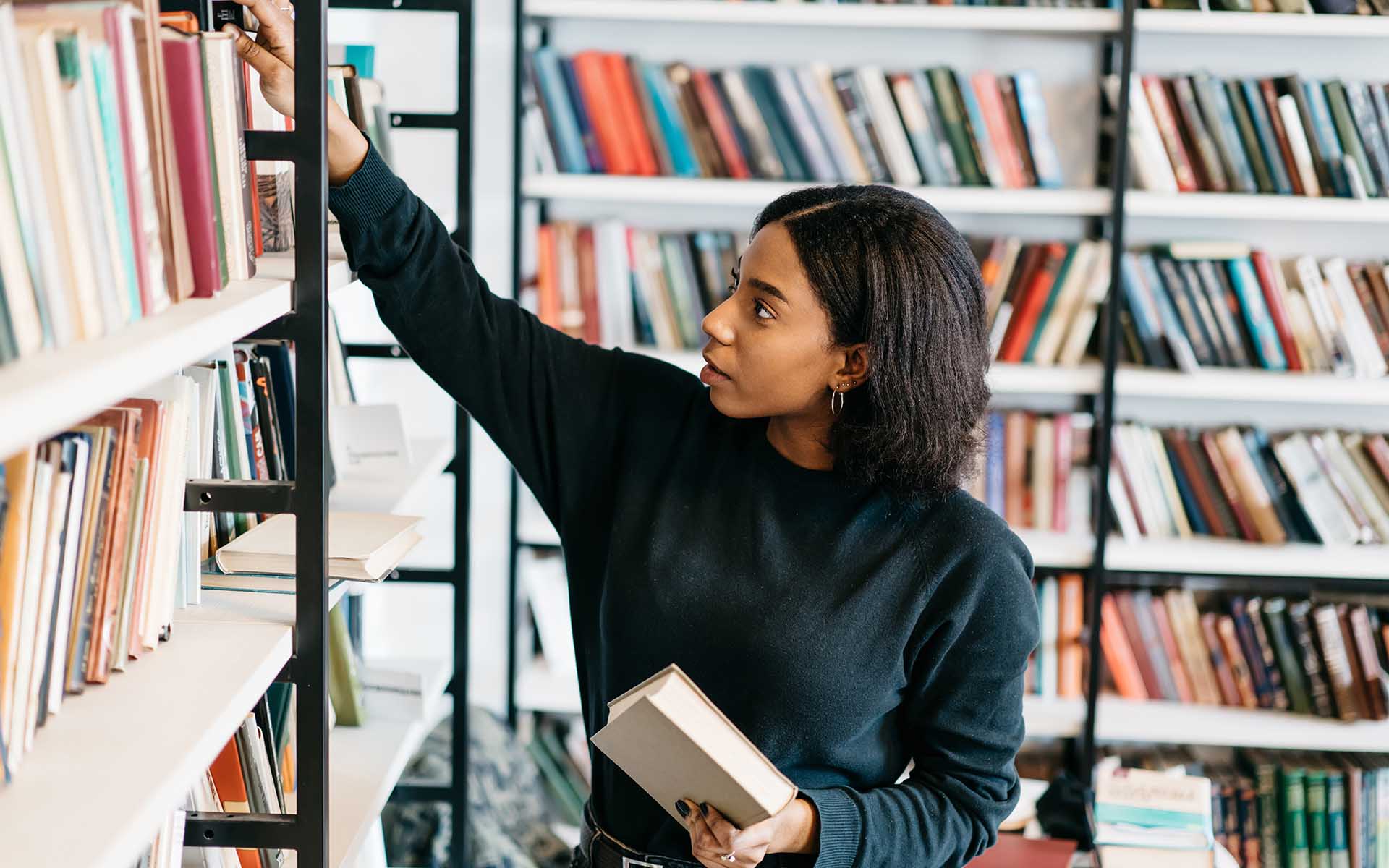 Young female african american librarian making order on bookshelf.